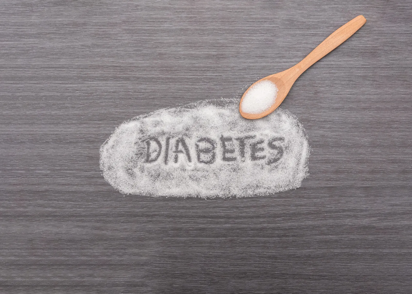 Das Wort Diabetes in einen Haufen Zucker geschrieben, daneben ein Holzlöffel mit Zucker