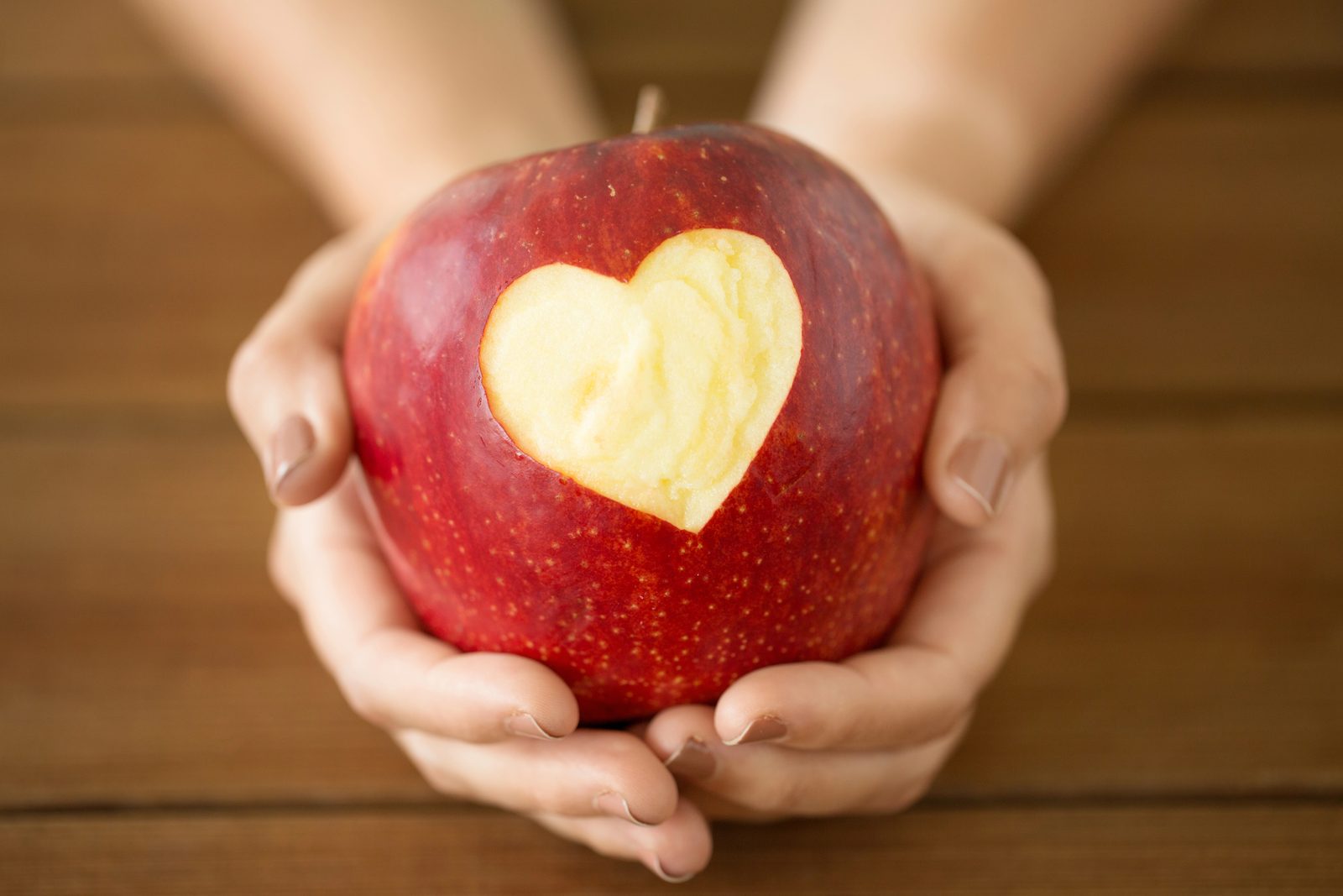 Hände halten einen roten Apfel mit ausgeschnittenem Herz – das Fastenbrechen nach der Fastenwoche
