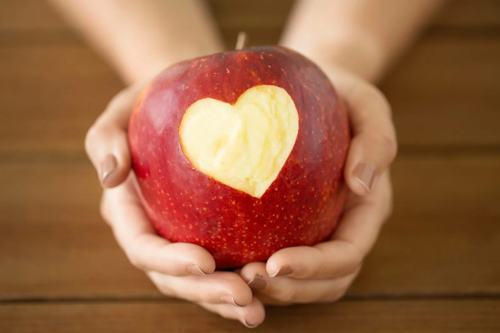 Hände halten einen roten Apfel mit ausgeschnittenem Herz – das Fastenbrechen nach der Fastenwoche