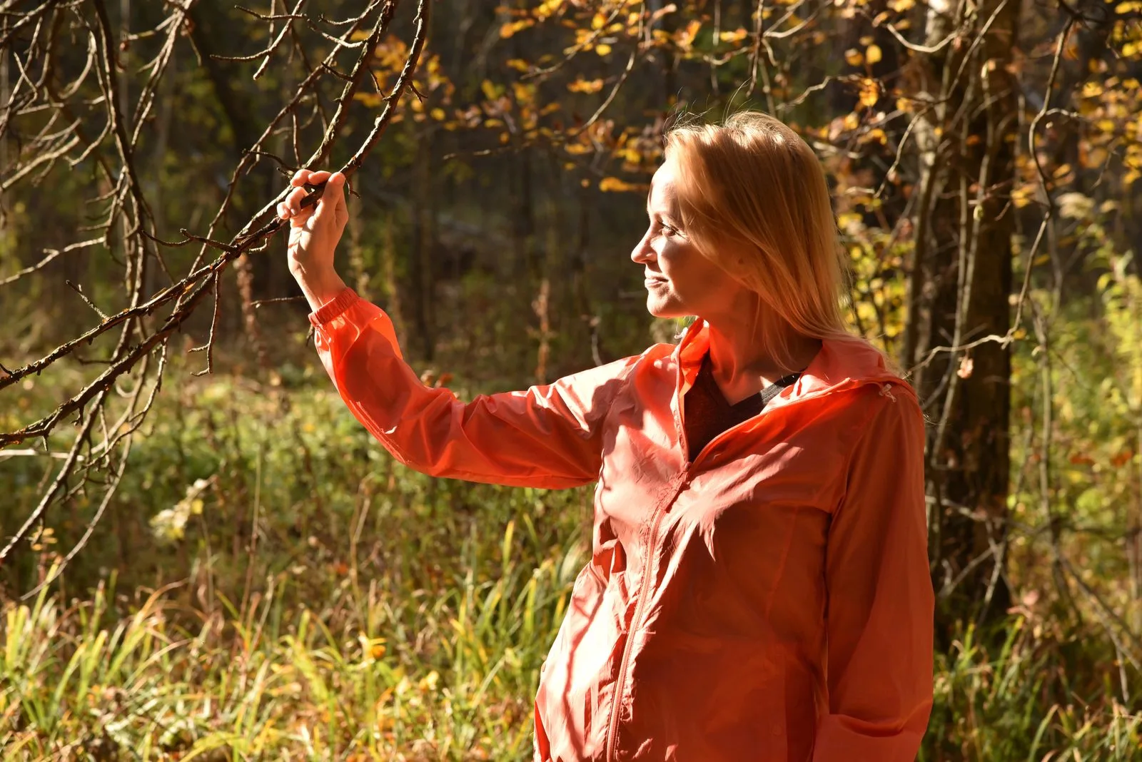 Frau in orangefarbener Jacke steht nachdenklich im herbstlichen Wald – die Fastenkrise überstehen